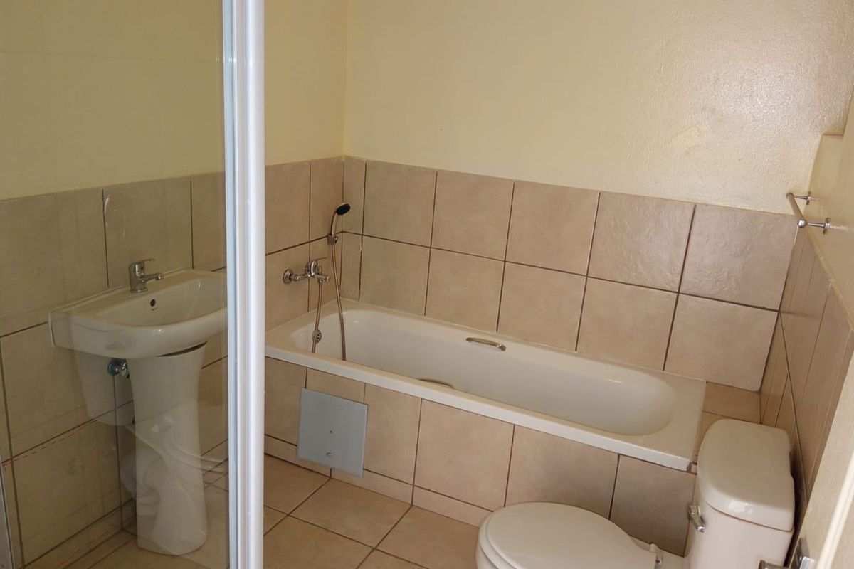 A functional bathroom featuring a pedestal basin, bathtub with handheld shower, and a separate shower enclosure with neutral wall and floor tiling.