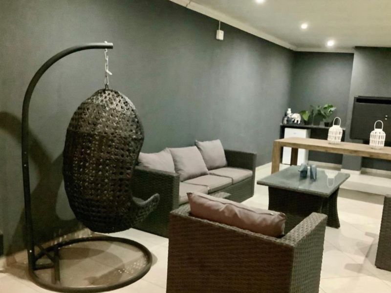 A covered patio area featuring tiled flooring, recessed downlighting, and a built-in fireplace, creating a comfortable space for outdoor relaxation.