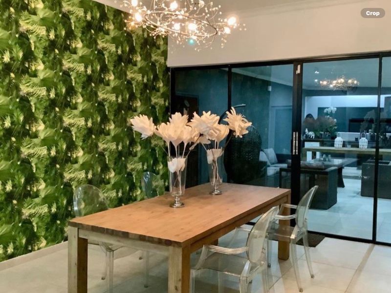 A contemporary dining area featuring a bold botanical feature wall, modern chandelier lighting, and large sliding glass doors leading to an outdoor space.