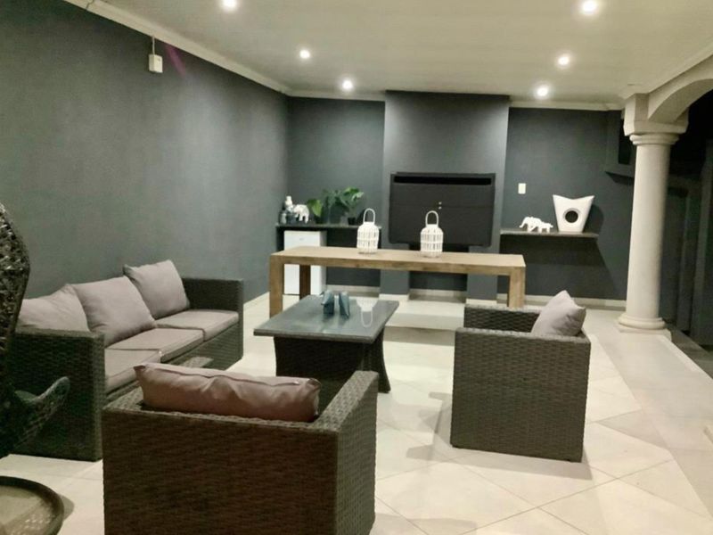 A covered outdoor patio area featuring a built-in fireplace, recessed lighting, and tiled flooring, ideal for evening entertaining.