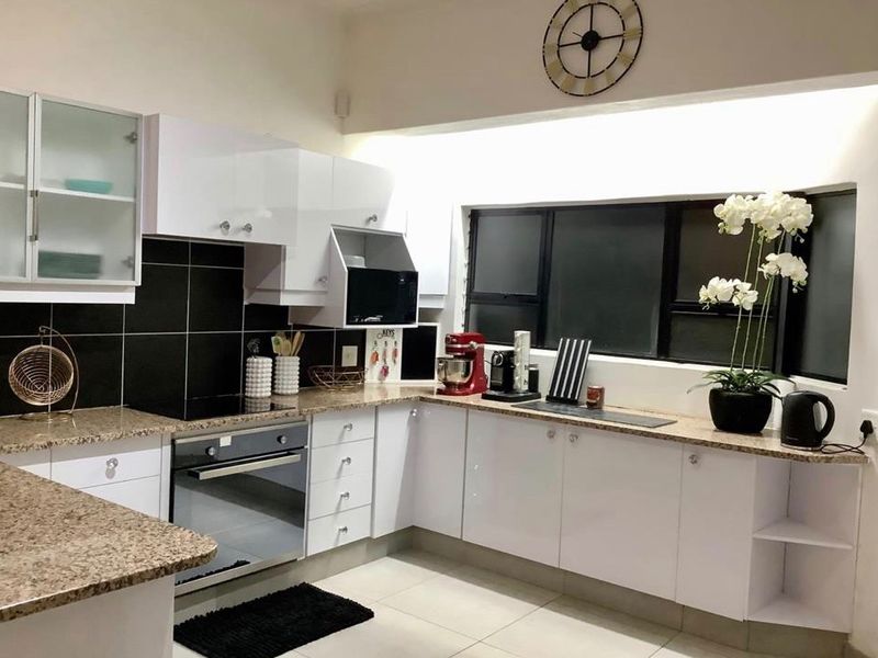 Modern kitchen featuring white gloss cabinetry, granite countertops, a built-in oven, and a sleek black tiled splashback.