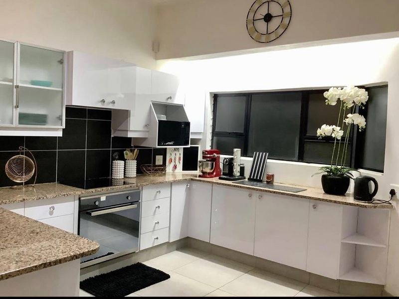 Modern kitchen featuring white high-gloss cabinetry, granite countertops, a black tiled backsplash, and integrated appliances including an oven and hob.