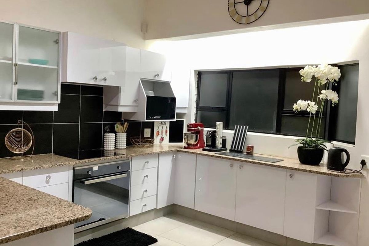 Modern kitchen featuring white high-gloss cabinetry, granite countertops, a black tiled backsplash, and integrated appliances including an oven and hob.