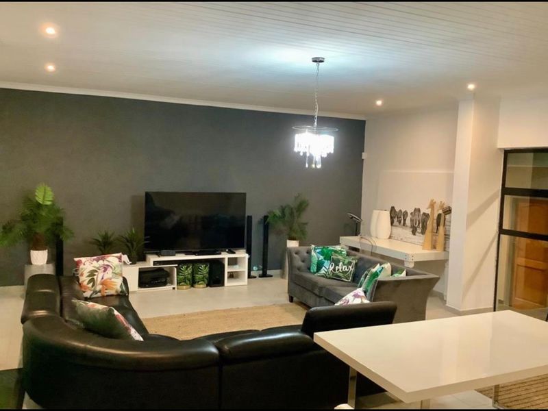 A spacious living room featuring tiled flooring, a decorative beaded ceiling, recessed downlighting, and a dark accent wall.
