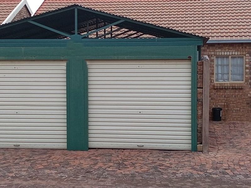Exterior view of a double garage with roller doors, featuring a brick facade, tiled roof, and paved driveway area.