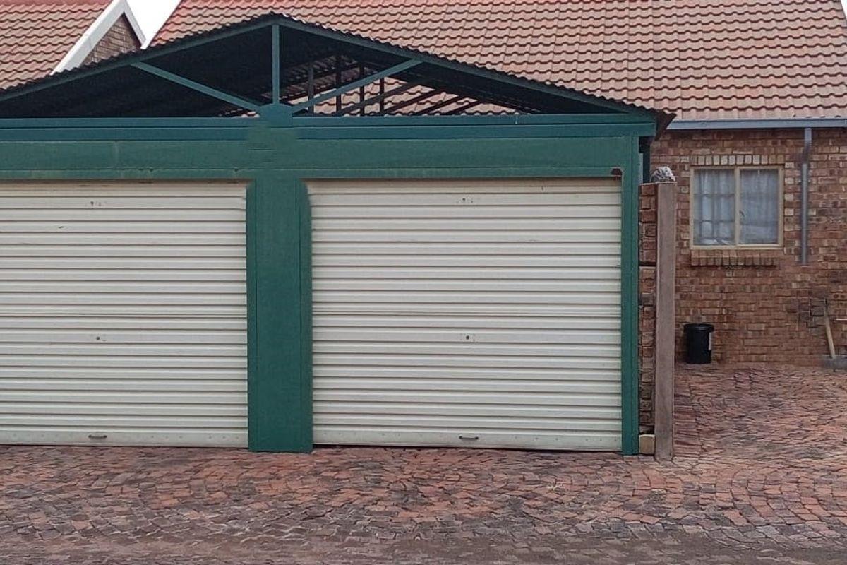 Exterior view of a double garage with roller doors, featuring a brick facade, tiled roof, and paved driveway area.