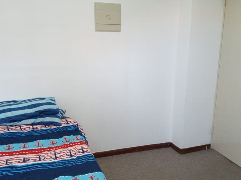 A simple bedroom featuring carpeted flooring, neutral walls, and a visible electrical distribution board.