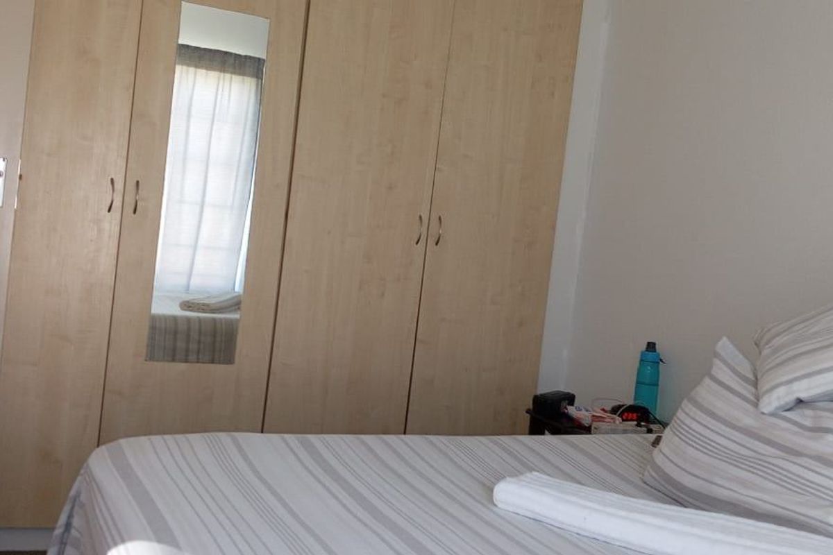 A bedroom featuring light wood-finish built-in wardrobes with an integrated mirror.