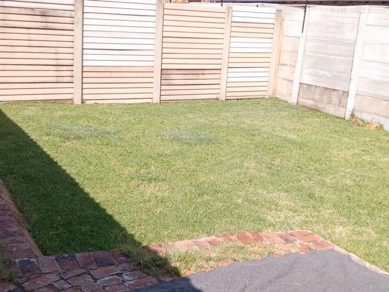 A private backyard garden featuring a lawn area, brick paved border, and perimeter precast concrete walling.