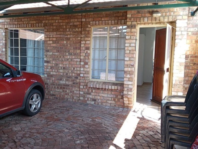 Front exterior view of a townhouse featuring a face brick facade, paved driveway, and a covered carport area.