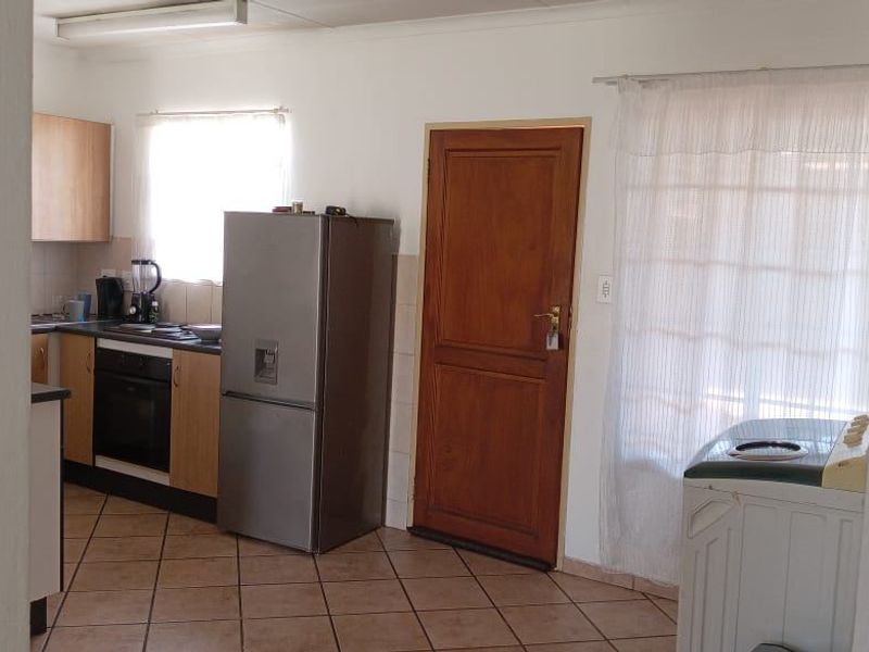 A functional kitchen area featuring built-in cabinetry, an integrated oven and hob, tiled flooring, and direct access to an exterior door.