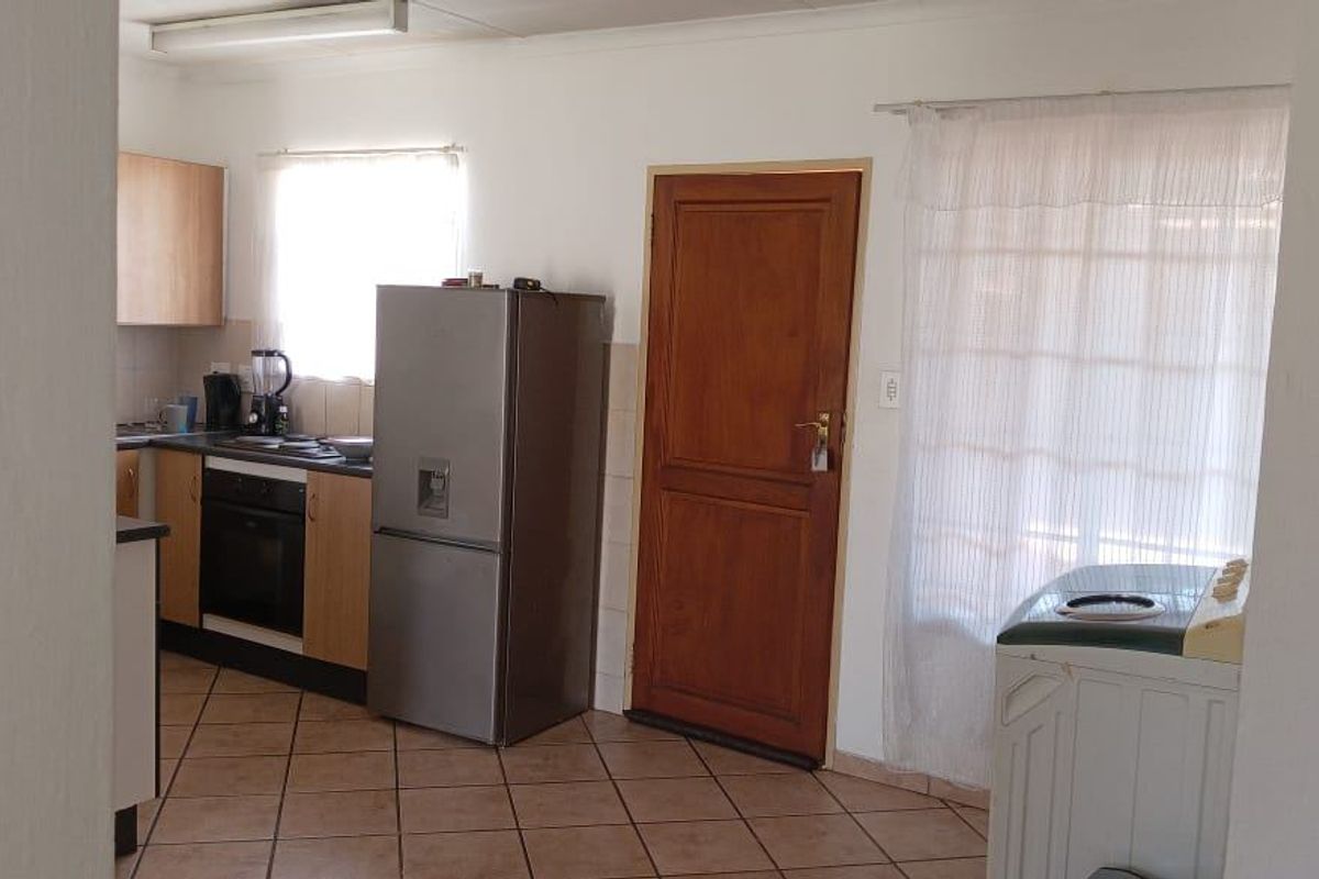 A functional kitchen area featuring built-in cabinetry, an integrated oven and hob, tiled flooring, and direct access to an exterior door.