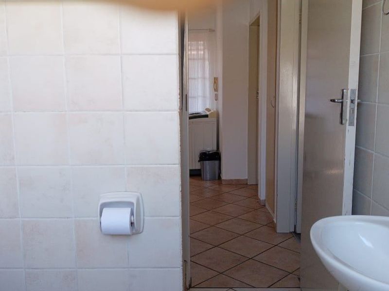 A functional bathroom featuring ceramic wall tiling, a pedestal basin, and tiled flooring, with a view into the adjacent hallway.