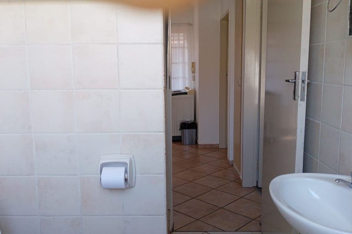 A functional bathroom featuring ceramic wall tiling, a pedestal basin, and tiled flooring, with a view into the adjacent hallway.