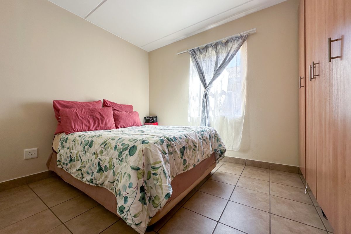 A functional bedroom featuring neutral wall tones, tiled flooring, and a built-in wooden wardrobe providing ample storage space.