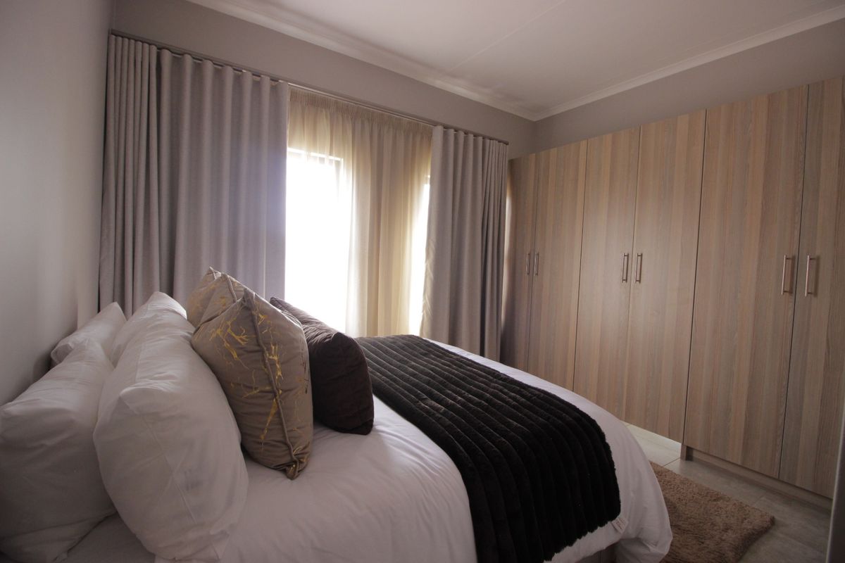 A well-maintained bedroom featuring neutral tones, ample built-in cupboard storage, and large windows with fitted curtain tracks.