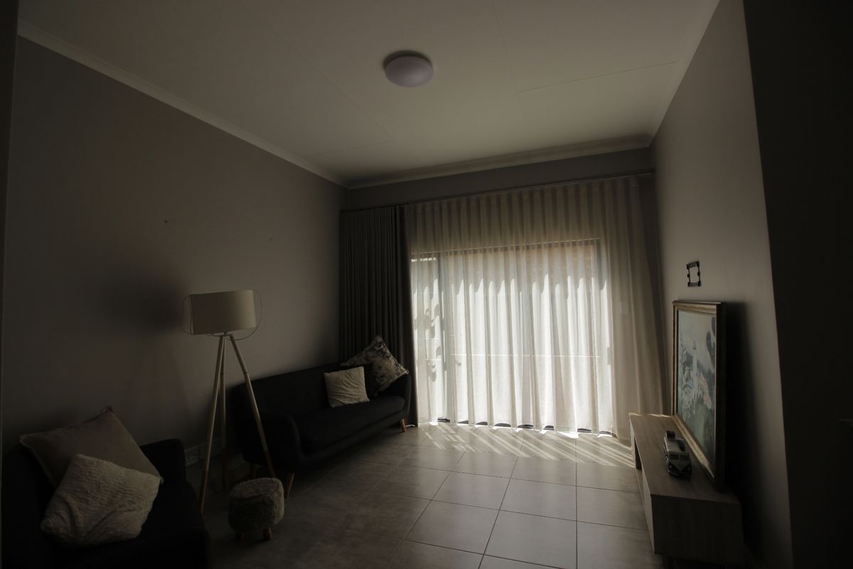 A living room featuring tiled flooring and a large sliding glass door with curtains, providing natural light to the space.