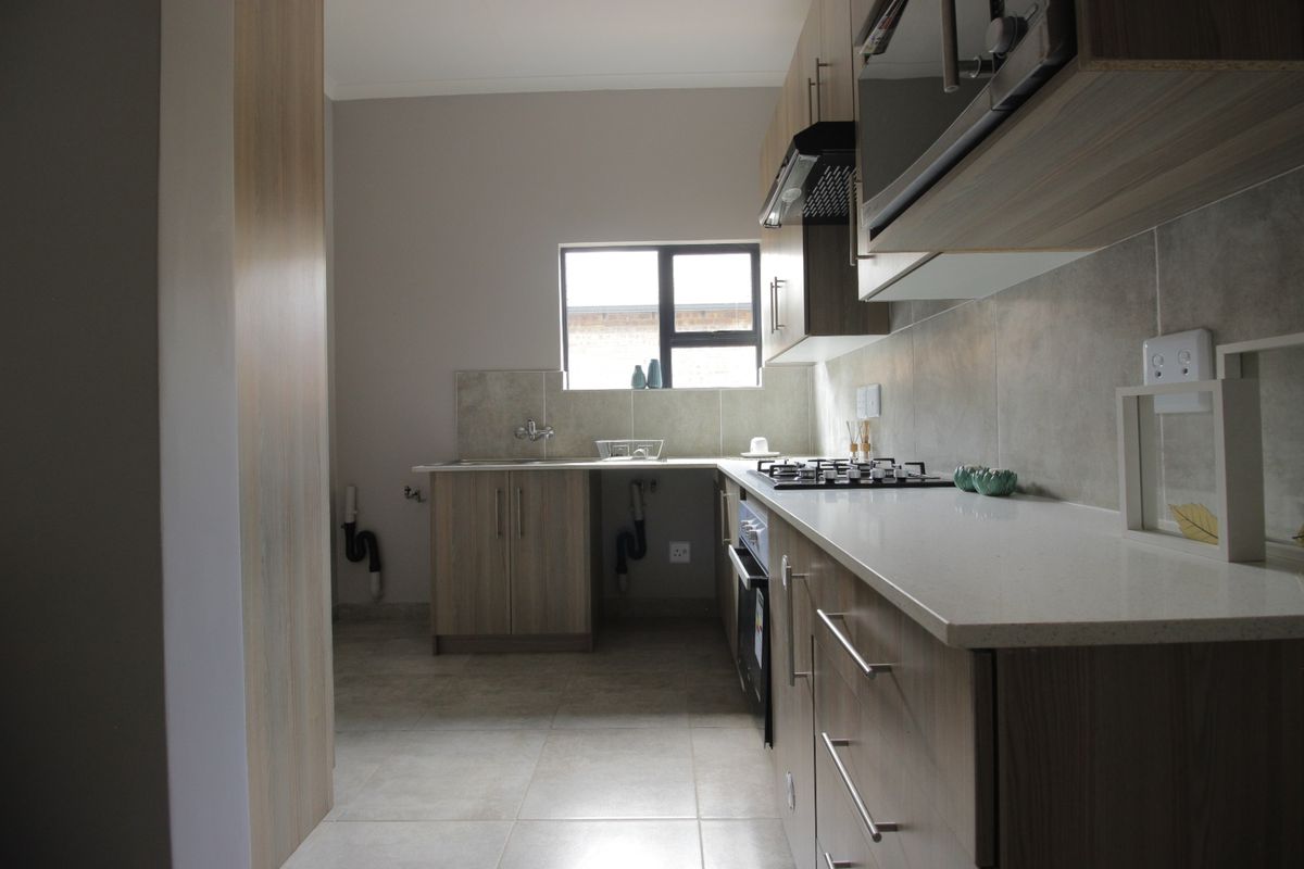 Modern kitchen featuring wood-finish cabinetry, stone countertops, a gas hob, built-in oven, and neutral tiled flooring with a functional layout.