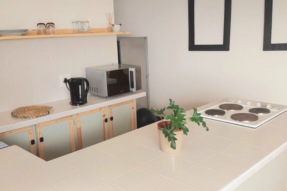 A functional kitchen featuring tiled countertops, a built-in electric hob, and a stainless steel sink with open shelving for storage.
