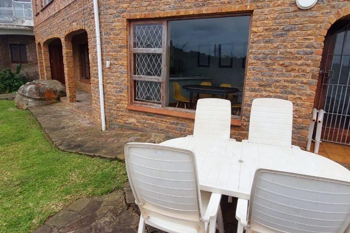 Rear exterior view of a brick-clad house featuring a stone-paved patio area and access to the garden.