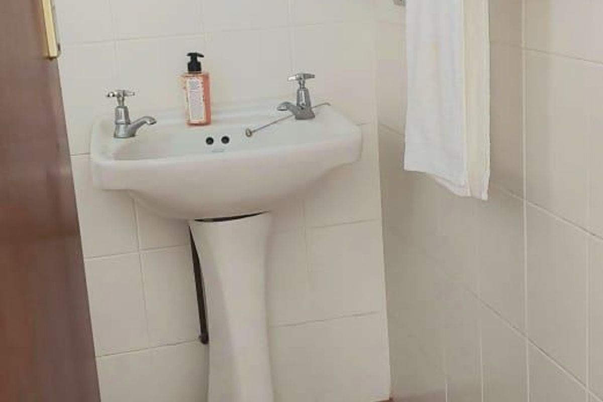 A compact bathroom featuring a white pedestal basin, tiled wall finishes, and ceramic floor tiles.
