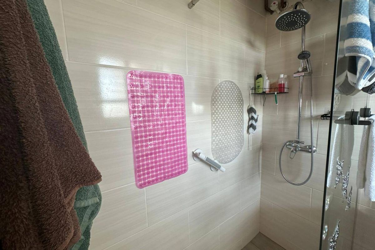 A functional shower enclosure featuring modern wall tiling, a rain shower head, and a glass screen.