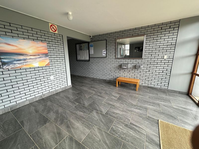 A clean and modern apartment entrance lobby featuring grey brick-style wall cladding and large format floor tiles.