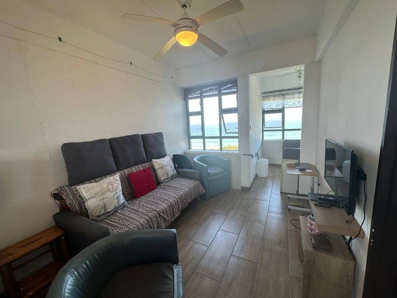 Living room featuring tiled flooring, a ceiling fan, and large windows with ocean views. The space requires cosmetic updates to the wall finishes.