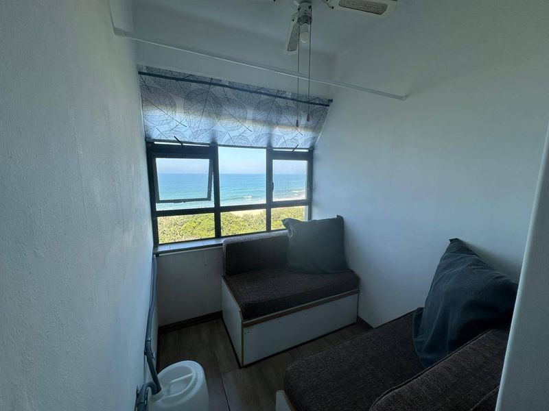 Enclosed balcony area featuring laminate flooring, a ceiling fan, and large windows offering direct ocean views.