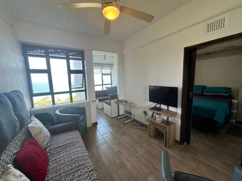 Living room featuring tiled flooring, a ceiling fan, and large windows with ocean views, leading into an adjacent bedroom and sunroom area.