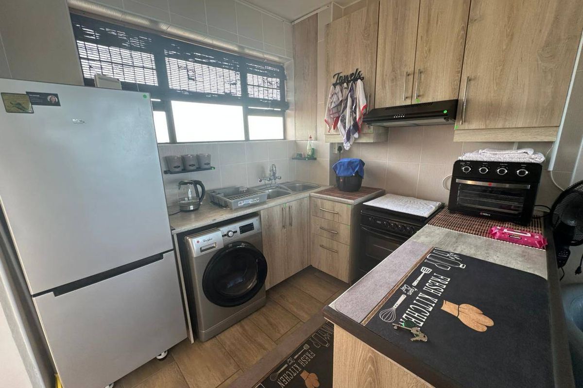 Compact kitchen featuring light wood-look cabinetry, tiled backsplash, integrated sink, and functional layout with space for laundry and cooking appliances.