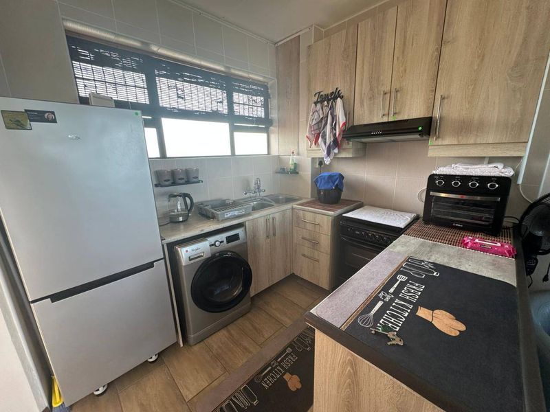 Compact kitchen featuring light wood-look cabinetry, tiled backsplash, integrated sink, and functional layout with space for laundry and cooking appliances.