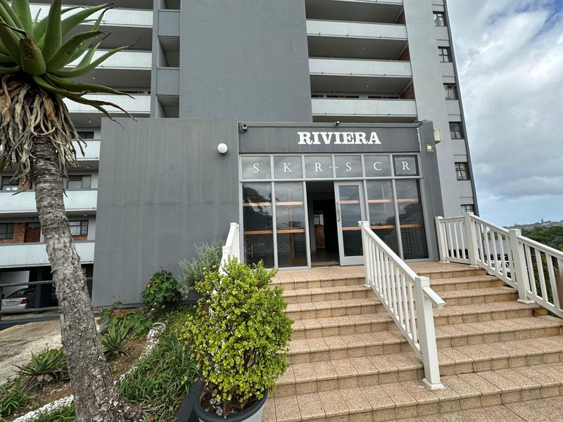 The front entrance of the Riviera apartment building, featuring a tiled staircase with white balustrades leading to glass entry doors.