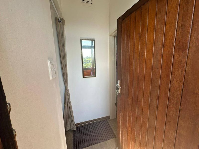 A functional apartment entryway featuring a solid timber door, neutral wall finishes, and a small window providing natural light.