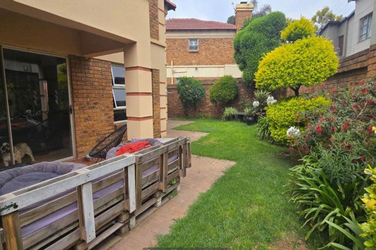 A rear view of the property featuring a paved patio area, sliding glass doors, and a well-maintained landscaped garden with brick boundary walls.
