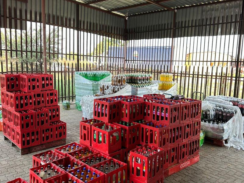 A covered industrial utility or storage area featuring a corrugated metal roof, steel support structure, and paved flooring, enclosed by metal security fencing.