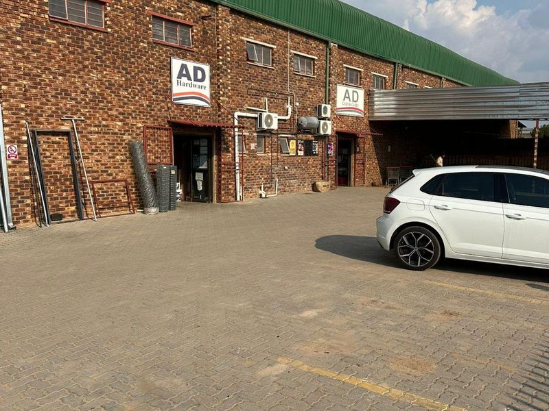Front elevation of an industrial warehouse building featuring exposed brickwork, a green corrugated roof, and a paved parking area.