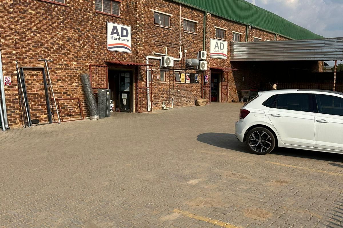 Front elevation of an industrial warehouse building featuring exposed brickwork, a green corrugated roof, and a paved parking area.