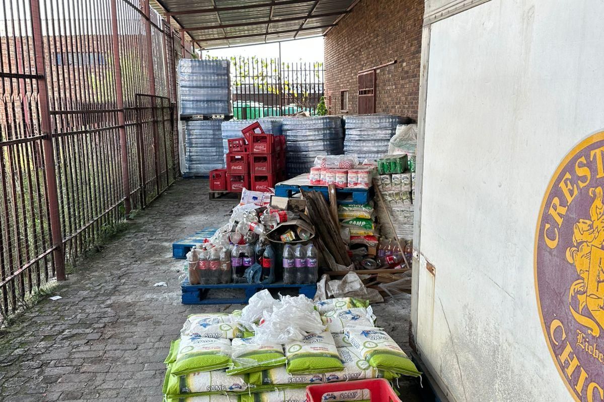 Covered outdoor utility or storage area featuring a corrugated metal roof, brick wall, and paved flooring, currently used for industrial storage.
