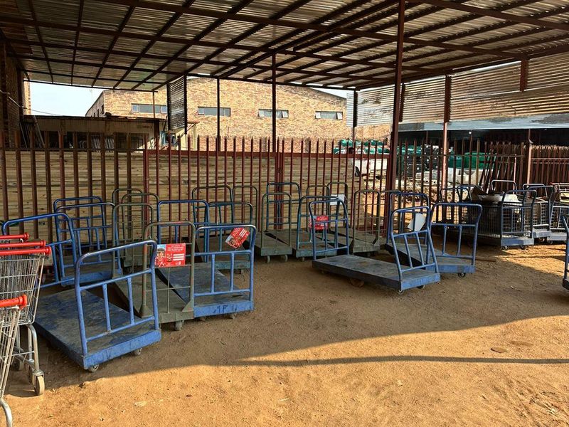 An industrial utility area featuring a covered structure with a corrugated metal roof, steel supports, and perimeter fencing over an unpaved ground surface.