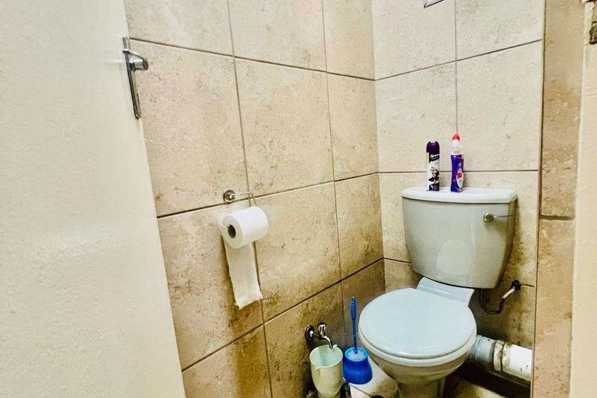 A compact bathroom featuring floor-to-ceiling beige tiling, a standard toilet, and a small top-hung window for ventilation.