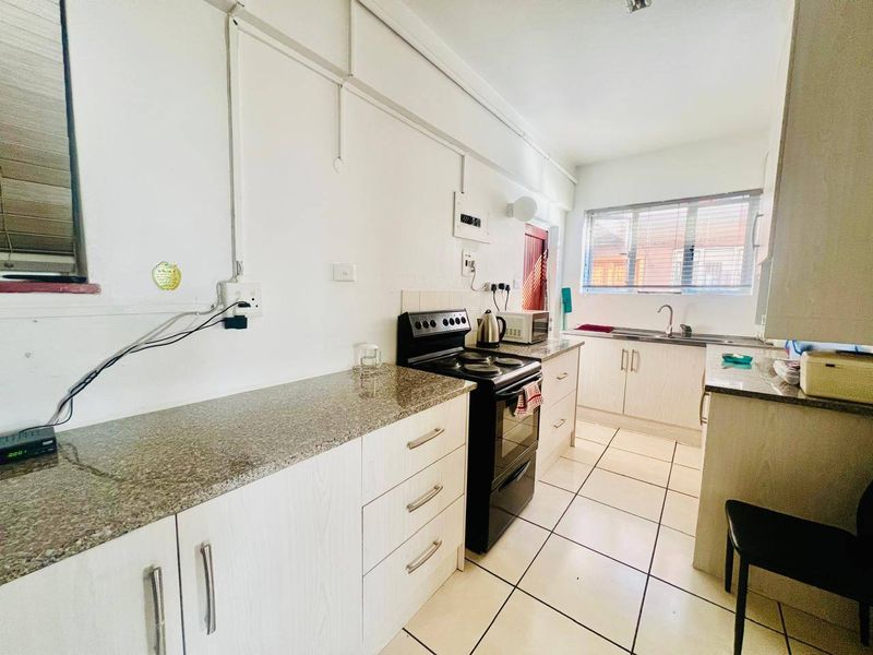 Functional kitchen featuring granite countertops, light-toned cabinetry, ceramic floor tiles, and a freestanding stove with exposed electrical conduit.