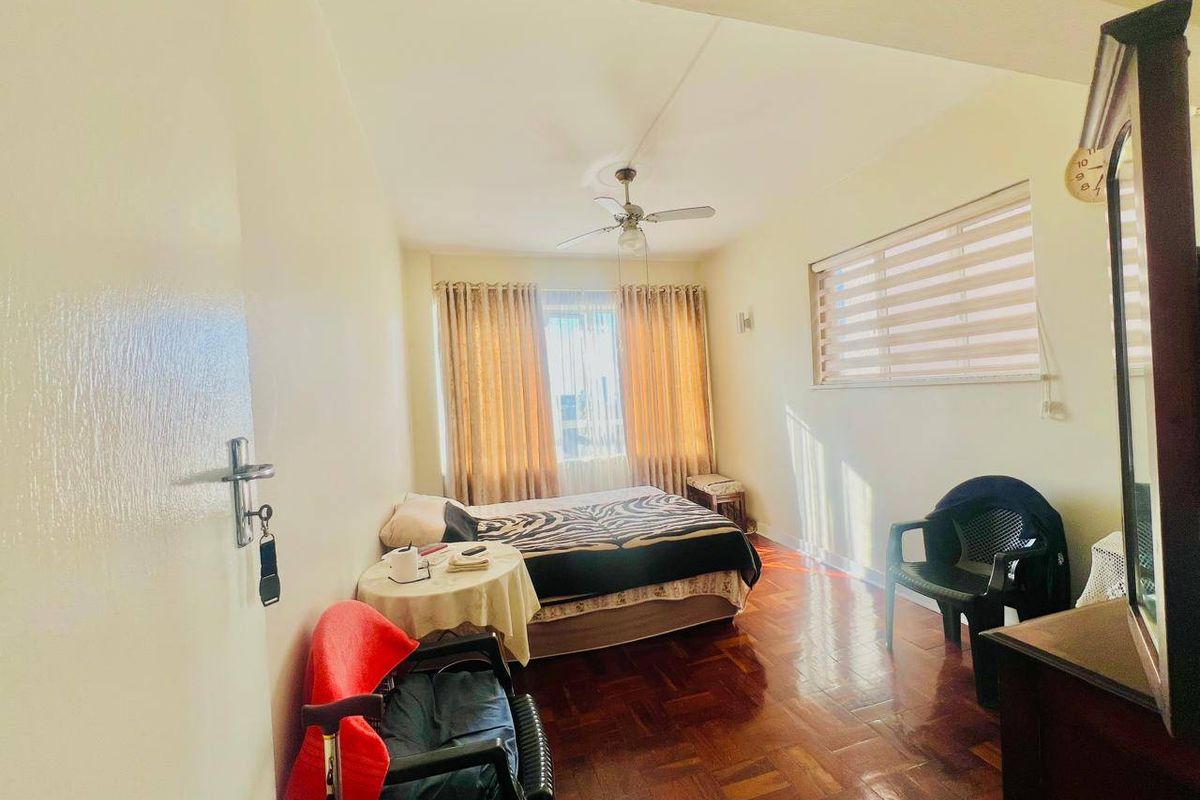 A bedroom featuring parquet flooring, a ceiling fan, and window blinds, offering a functional space with potential for modern updates.
