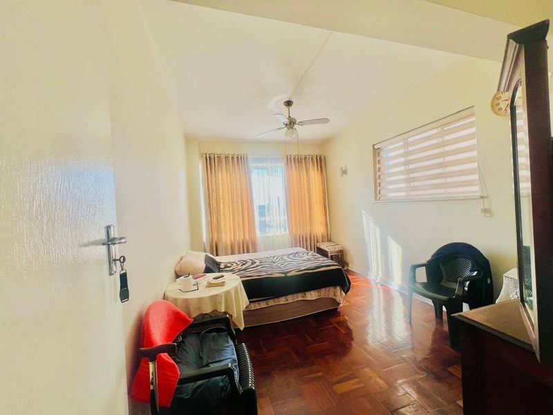 A bedroom featuring parquet flooring, a ceiling fan, and window blinds, offering a functional space with potential for modern updates.
