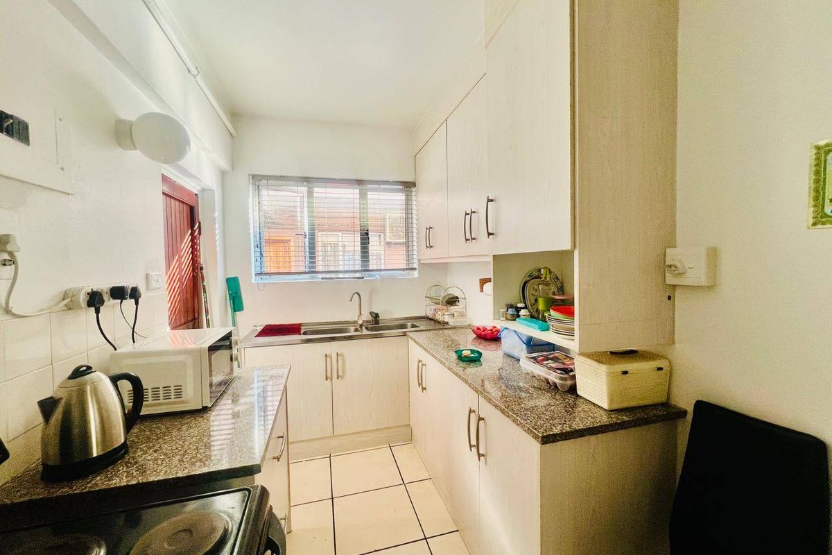 A functional galley-style kitchen featuring laminate cabinetry, granite countertops, stainless steel sink, and ceramic floor tiles with natural light from a window.