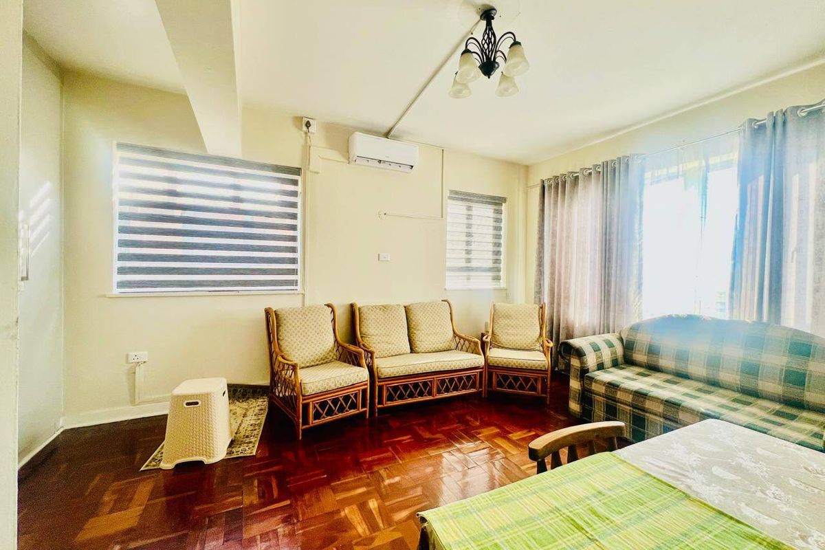 A living room featuring polished parquet flooring, a wall-mounted air conditioning unit, and multiple windows with fitted blinds and curtains.