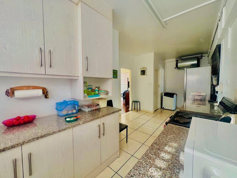 Functional kitchen featuring laminate cabinetry, granite countertops, and an electric stove, with tiled flooring throughout and direct access to the adjacent living area.