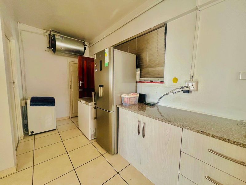 A functional kitchen area featuring granite countertops, light-toned cabinetry, and tiled flooring, with an exposed geyser and surface-mounted electrical conduits.