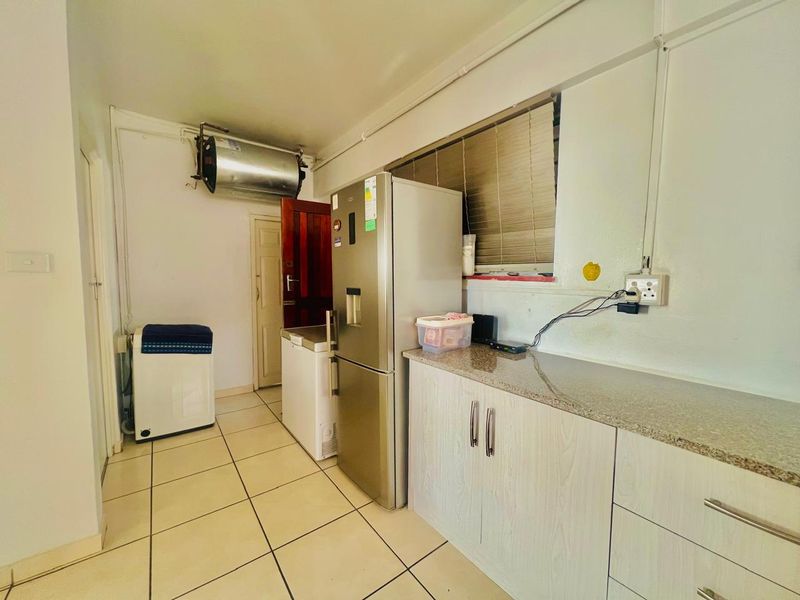 Functional laundry area featuring tiled flooring, granite countertops, built-in cabinetry, and an overhead electric geyser.