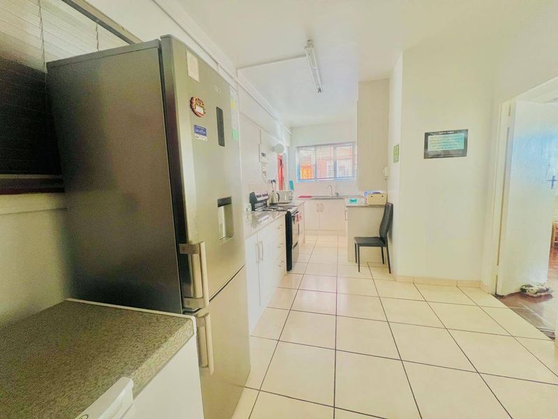 A functional kitchen featuring white cabinetry, laminate countertops, tiled flooring, and a freestanding stove, offering a clean and practical workspace.